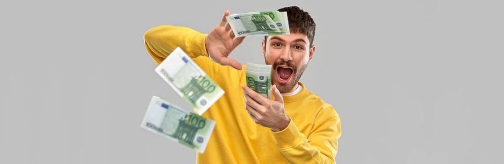 Foto für den Blogartikel "Getrennt lebender Ehemann macht Schulden - was soll ich tun?". Auf dem Bild ist ein junger Mann im gelben Pullover zu sehen, der mehrere 100-Euro-Scheine durch die Luft fliegen lässt und ausgelassen wirkt – ein Sinnbild für unbedachtes Geldausgeben und wachsende Schulden.