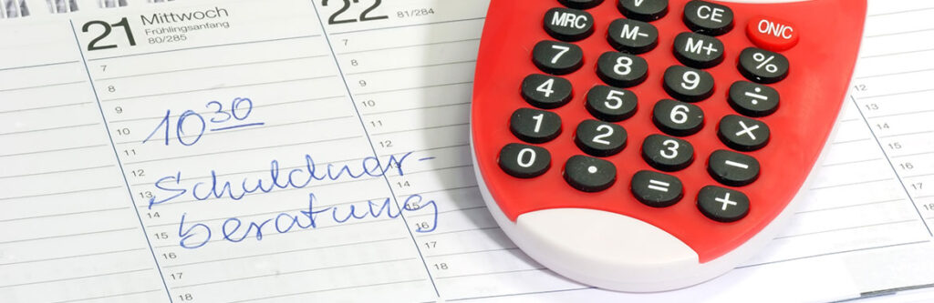 Foto für den Blogartikel "Termin bei der Schuldnerberatung - das sollten Sie wissen". Auf dem Foto sieht man einen Terminplaner mit handschriftlichem Eintrag "10:30 Uhr: Schuldnerberatung" neben rotem Taschenrechner - symbolisch für ein geplantes Beratungsgespräch bei Schulden.