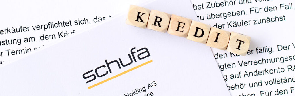 Foto für den Blogartikel "Umschuldung trotz Schufa?". Auf dem Foto sieht man ein SCHUFA-Dokument mit Holz-Würfeln "KREDIT" auf Vertragsseiten – Symbol für Umschuldung trotz negativer Schufa.