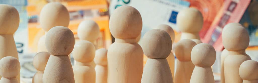 Foto für den Blogartikel "Gesamtschuldnerausgleich - was versteht man darunter?". Auf dem Foto: Holzfiguren auf Euro-Banknoten symbolisieren mehrere gemeinsam haftende Personen und die finanzielle Aufteilung von Forderungen beim Gesamtschuldnerausgleich.